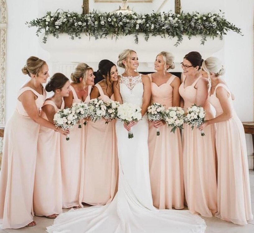 The bride and her bridesmaids smiling and laughing whilst holding their stunning bouquets whilst stood under a stunning floral arrangement
